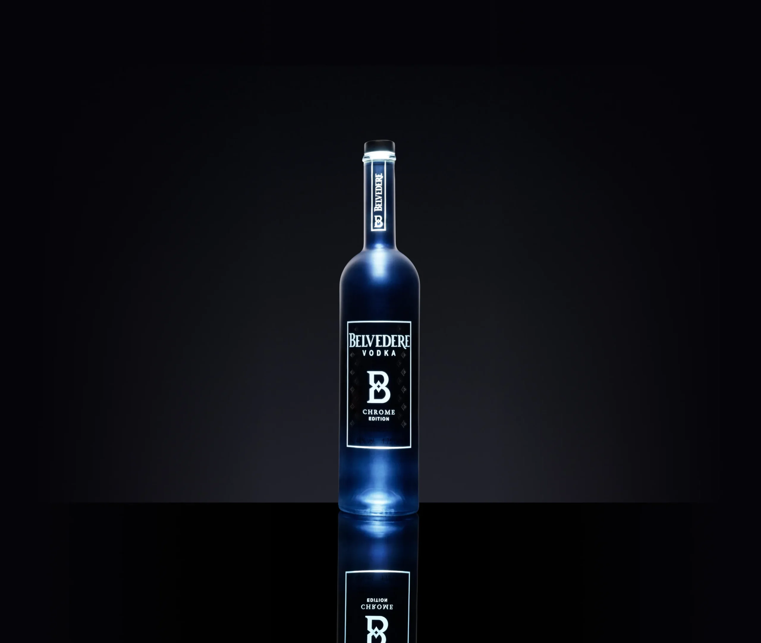 Superchouette- Une bouteille de vodka Belvedere avec une lueur bleue est centrée sur une surface noire réfléchissante sur un fond sombre. L'étiquette indique "Belvedere Vodka B Chrome".