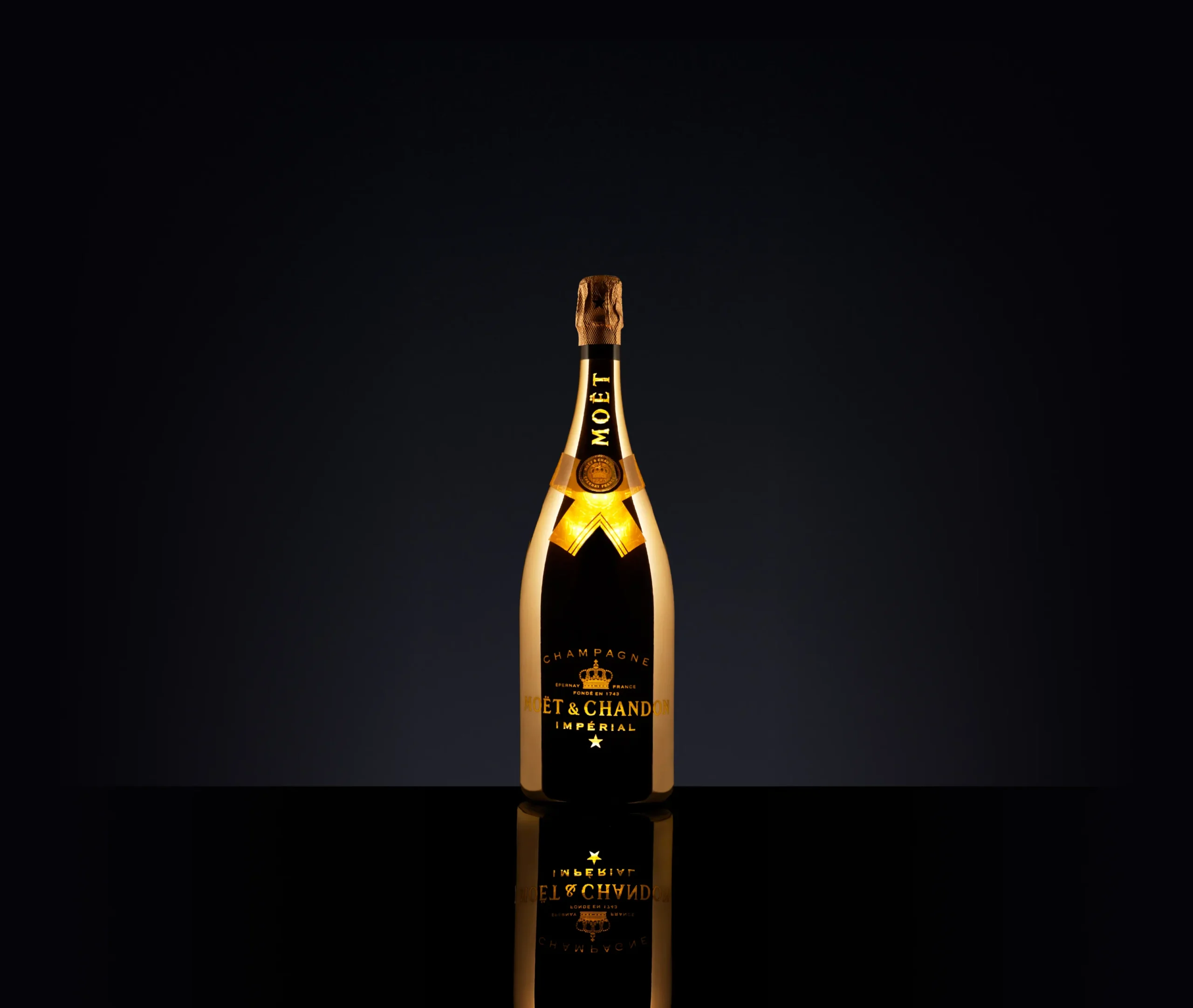 Superchouette- Une grande bouteille de champagne Moët & Chandon est éclairée sur un fond noir, créant un effet dramatique et élégant avec des reflets sur la surface brillante en dessous.
