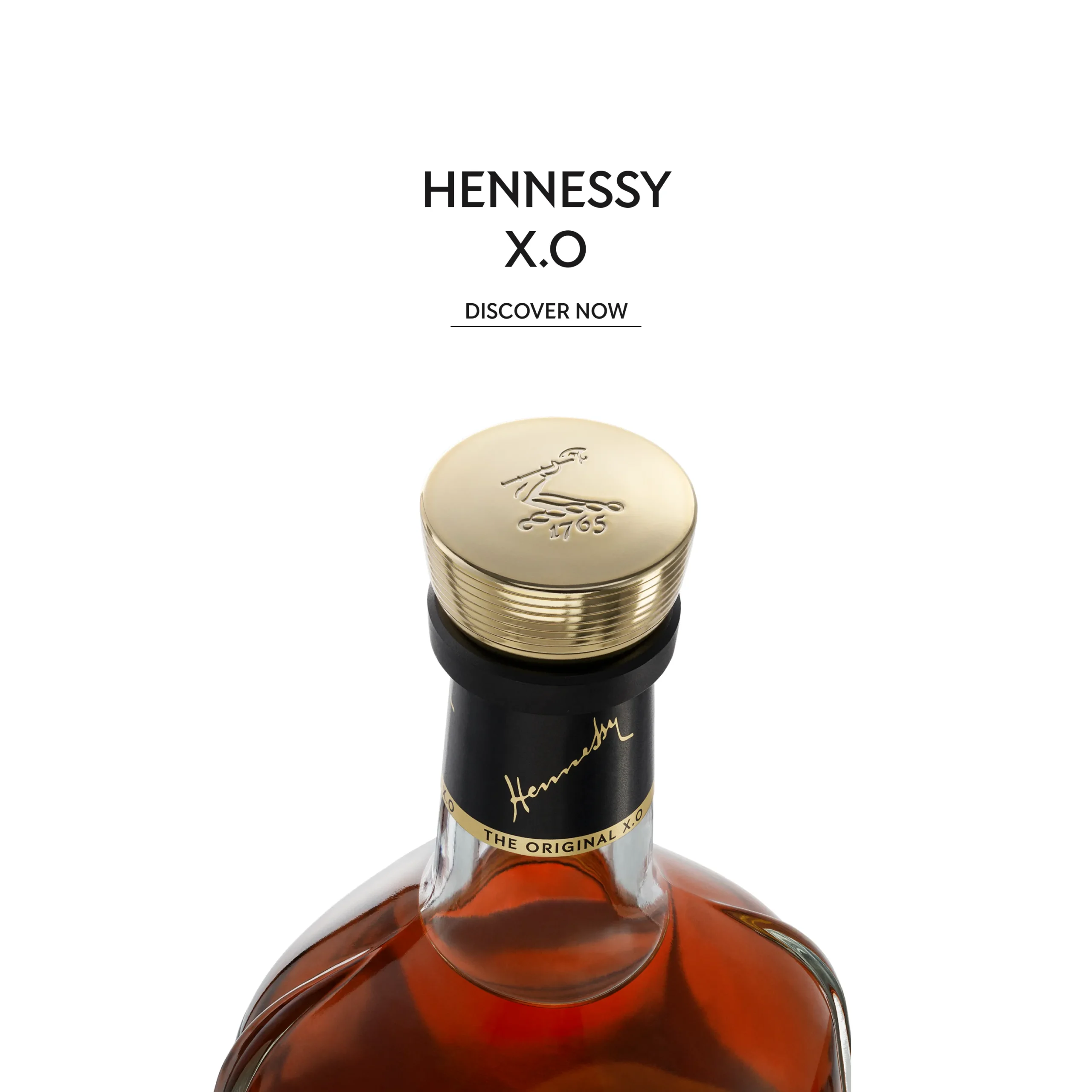 Superchouette- Gros plan d'une bouteille de cognac Hennessy X.O. avec un bouchon doré, une étiquette de col noire et un liquide ambré. Le texte au-dessus indique Hennessy X.O et Discover Now sur un fond blanc.