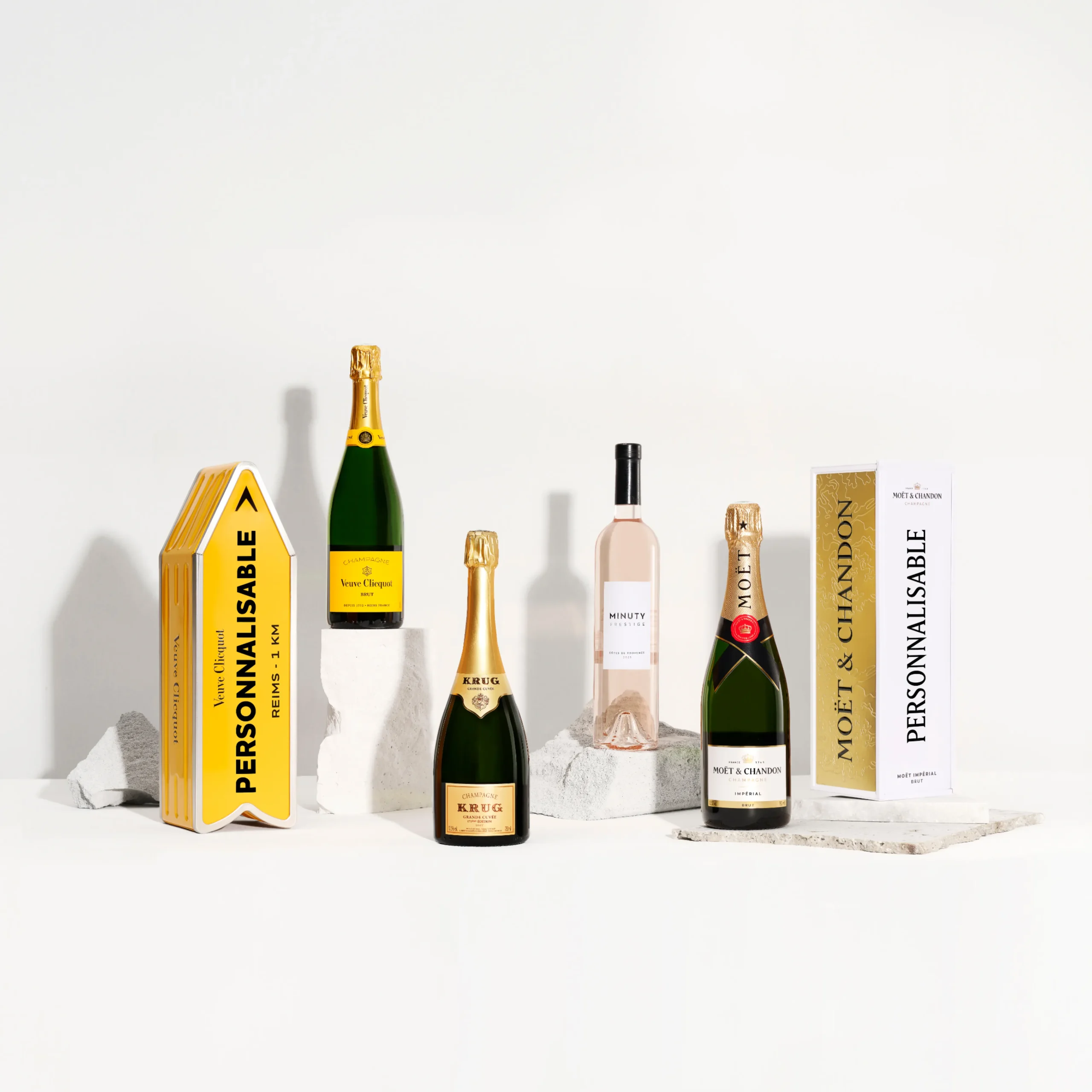 Superchouette- Cinq bouteilles de vin et de champagne, chacune avec son propre emballage, sont présentées sur des blocs de pierre blanche sur un fond blanc uni. L'emballage comporte des étiquettes à personnaliser.