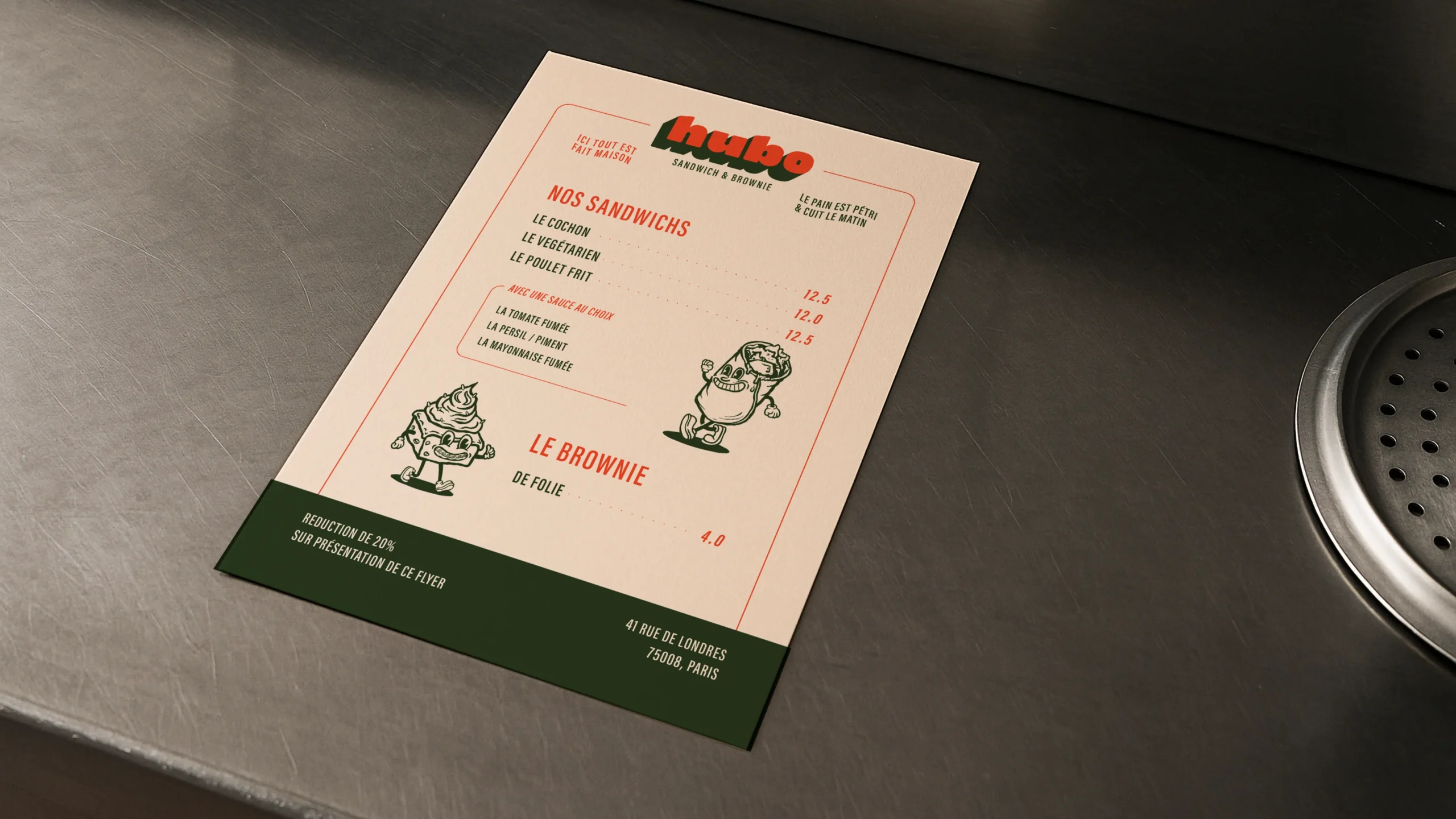 Superchouette- Un menu de sandwicherie imprimé sur un comptoir métallique énumère les sandwichs, un brownie, les prix, et présente des personnages de bande dessinée excentriques. Le nom et l'adresse de la boutique figurent également sur le menu.