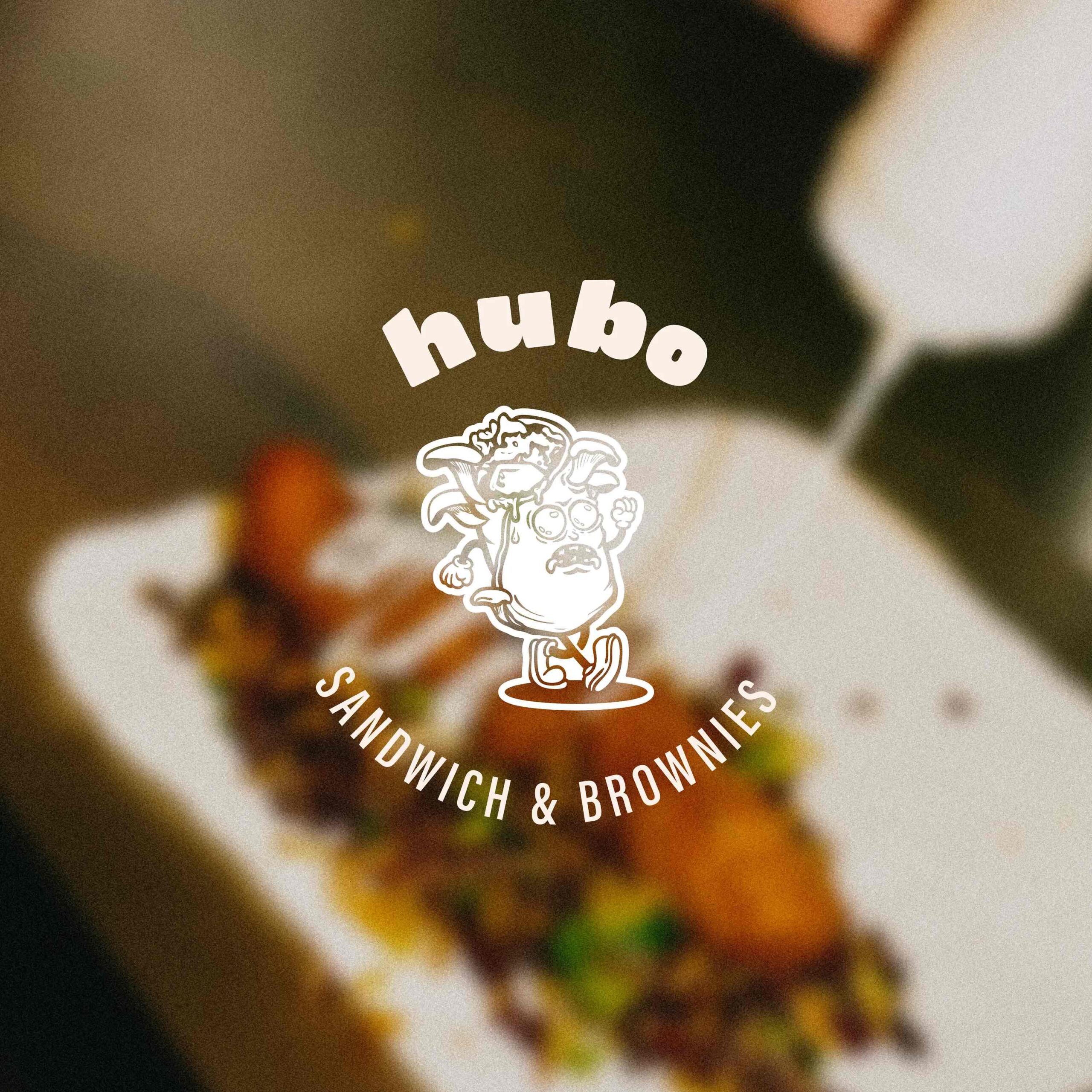 Superchouette- Image floue d'un plat de nourriture avec des ingrédients colorés sur une assiette blanche ; superposé avec le logo hubo SANDWICH & BROWNIES et un personnage de sandwich de bande dessinée au centre.